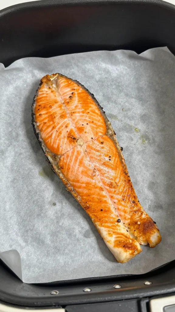 single golden air fryer salmon fillet on parchment-lined tray